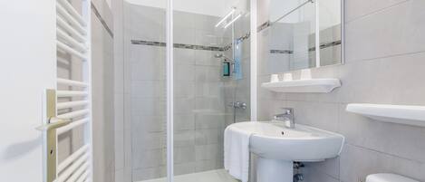 A modern bathroom with a glass-enclosed shower, a white sink, and a toilet.