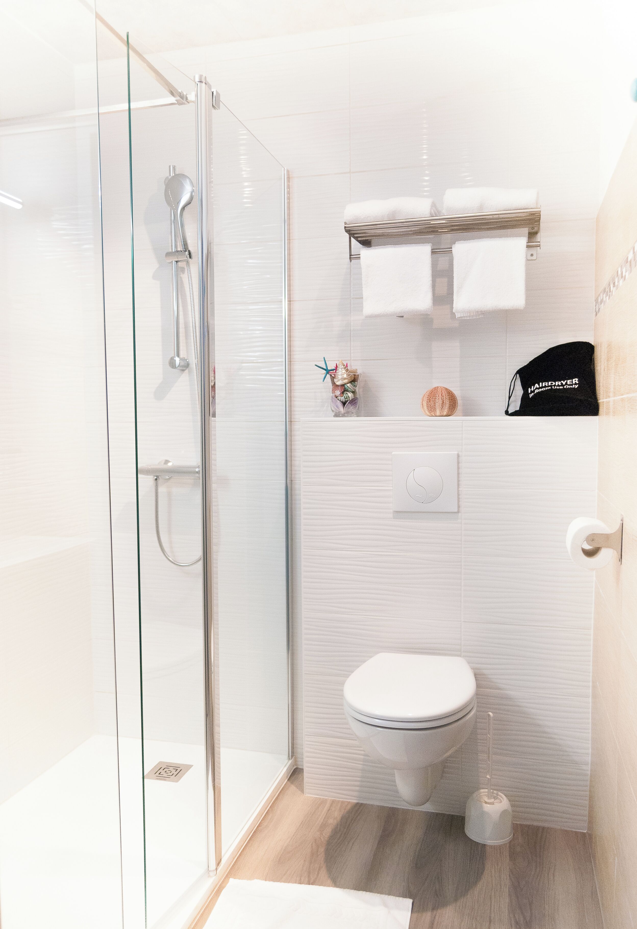 A modern bathroom with a glass shower enclosure, a toilet, and a towel rack with a hairdryer.