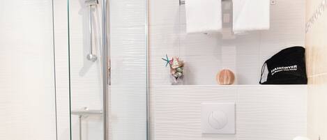 A modern bathroom with a glass shower enclosure, a toilet, and a towel rack with a hairdryer.