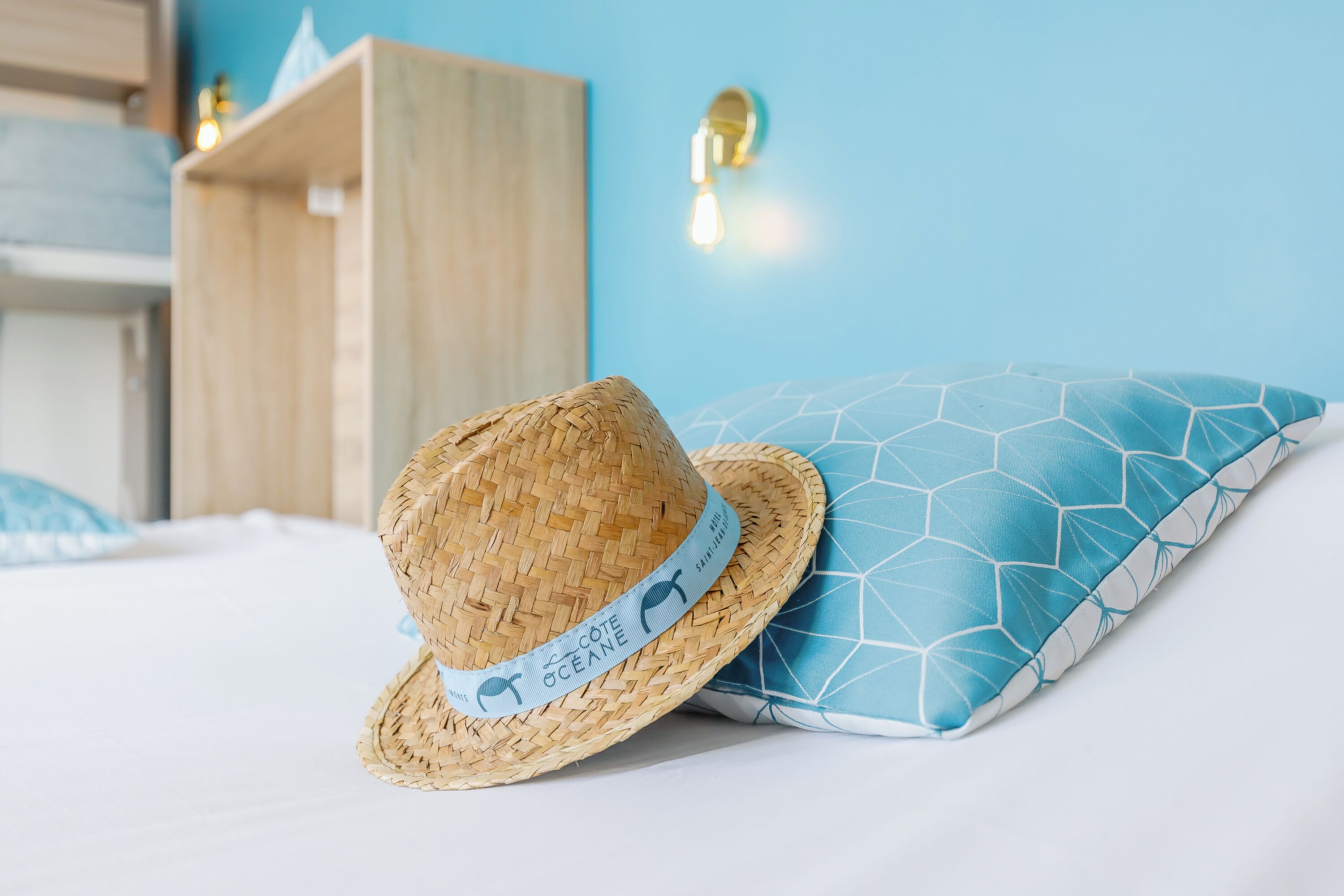 A straw hat with a label on a bed with a blue geometric pillow.
