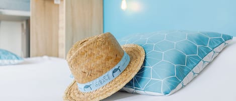 A straw hat with a label on a bed with a blue geometric pillow.