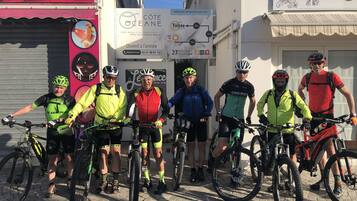 A group of cyclists standing in front of a building with a sign indicating the hotel name and amenities.