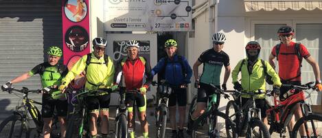 A group of cyclists standing in front of a building with a sign indicating the hotel name and amenities.