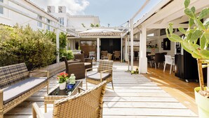 Une terrasse extérieure couverte, aménagée avec des meubles en osier, un coin repas et un cactus.