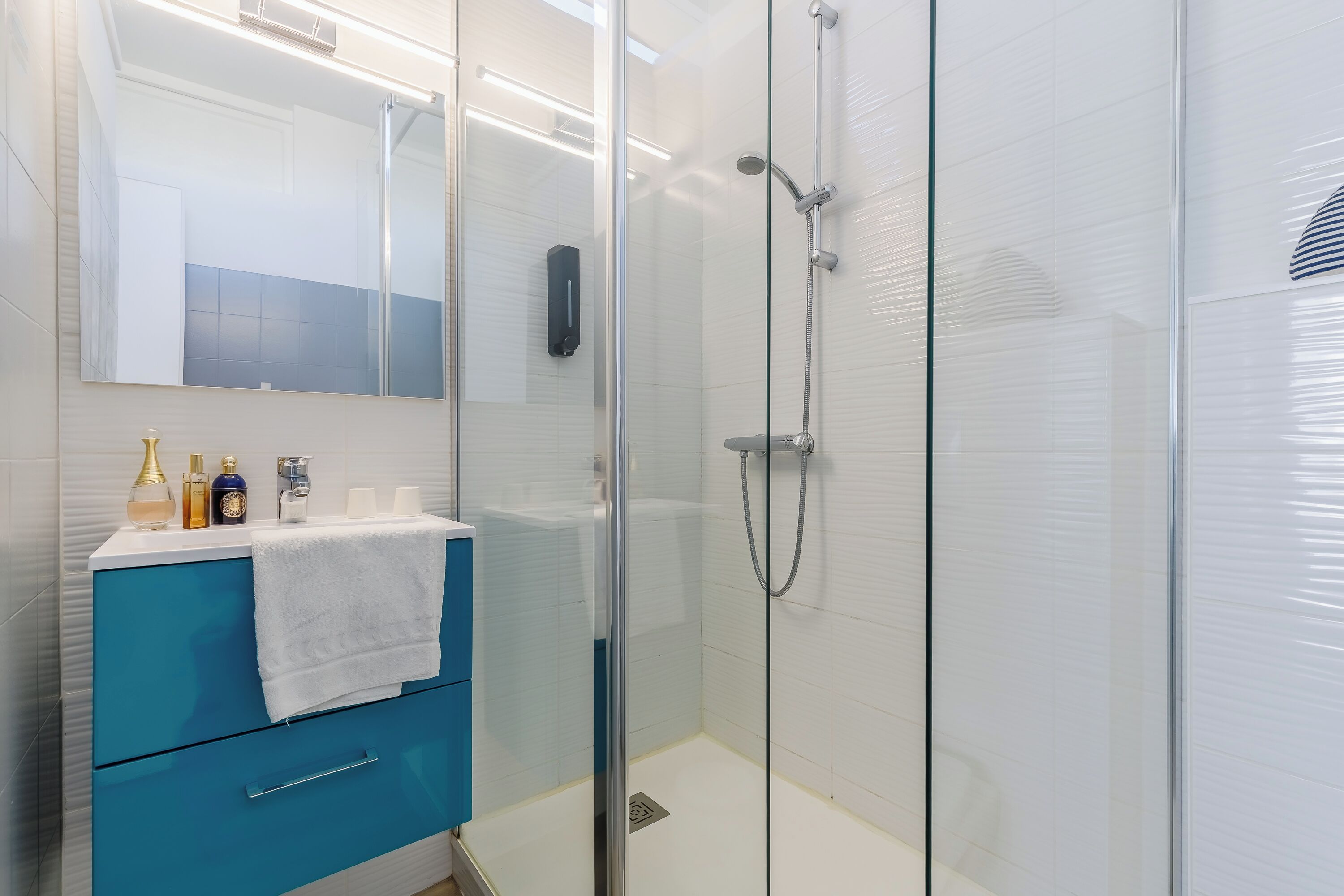A modern bathroom with a glass shower enclosure, a blue vanity with a white towel, and a mirror above the vanity.
