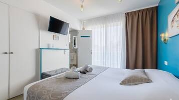 A hotel room with a bed, a TV mounted on the wall, a desk with a chair, and a window with curtains.