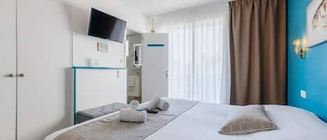 A hotel room with a bed, a TV mounted on the wall, a desk with a chair, and a window with curtains.