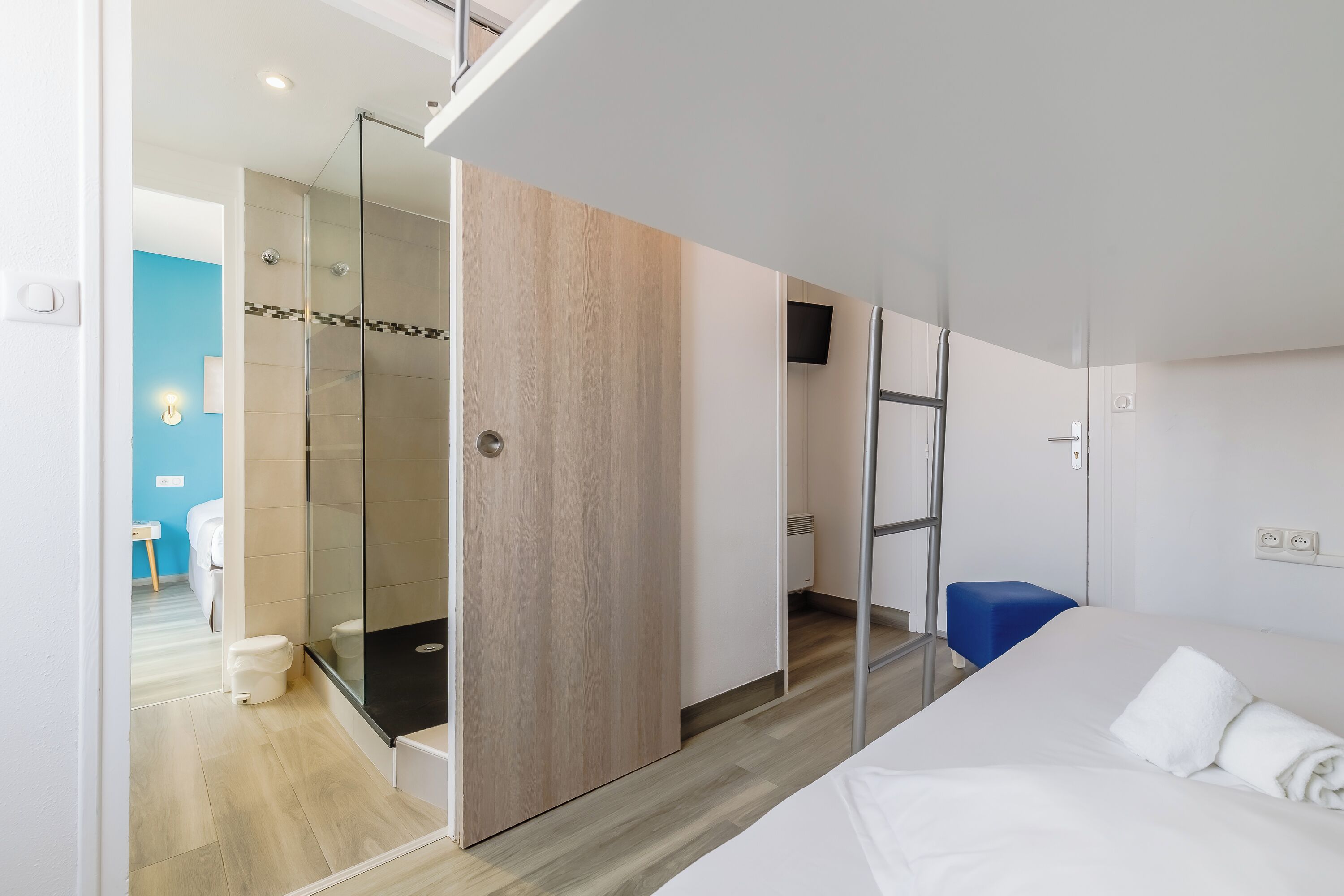 A modern hotel room with a bed, a shower area, and a blue chair.