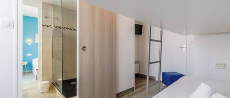 A modern hotel room with a bed, a shower area, and a blue chair.