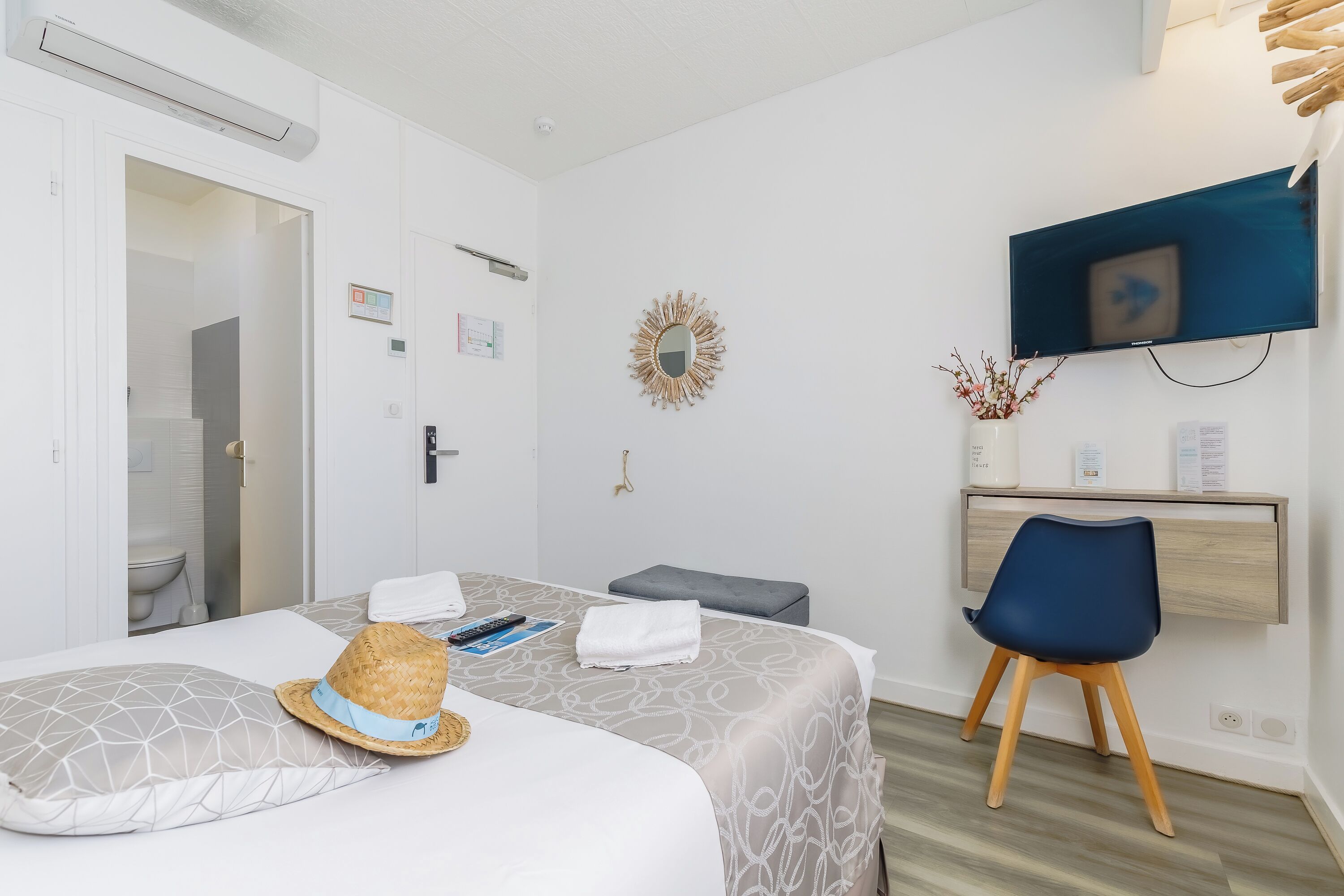 A hotel room with a bed, a desk, a TV, and a bathroom visible through an open door.