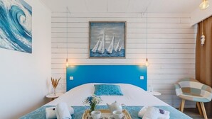 Une chambre d’hôtel avec un lit, un plateau avec un service à thé, un tableau représentant des voiliers et une chaise.