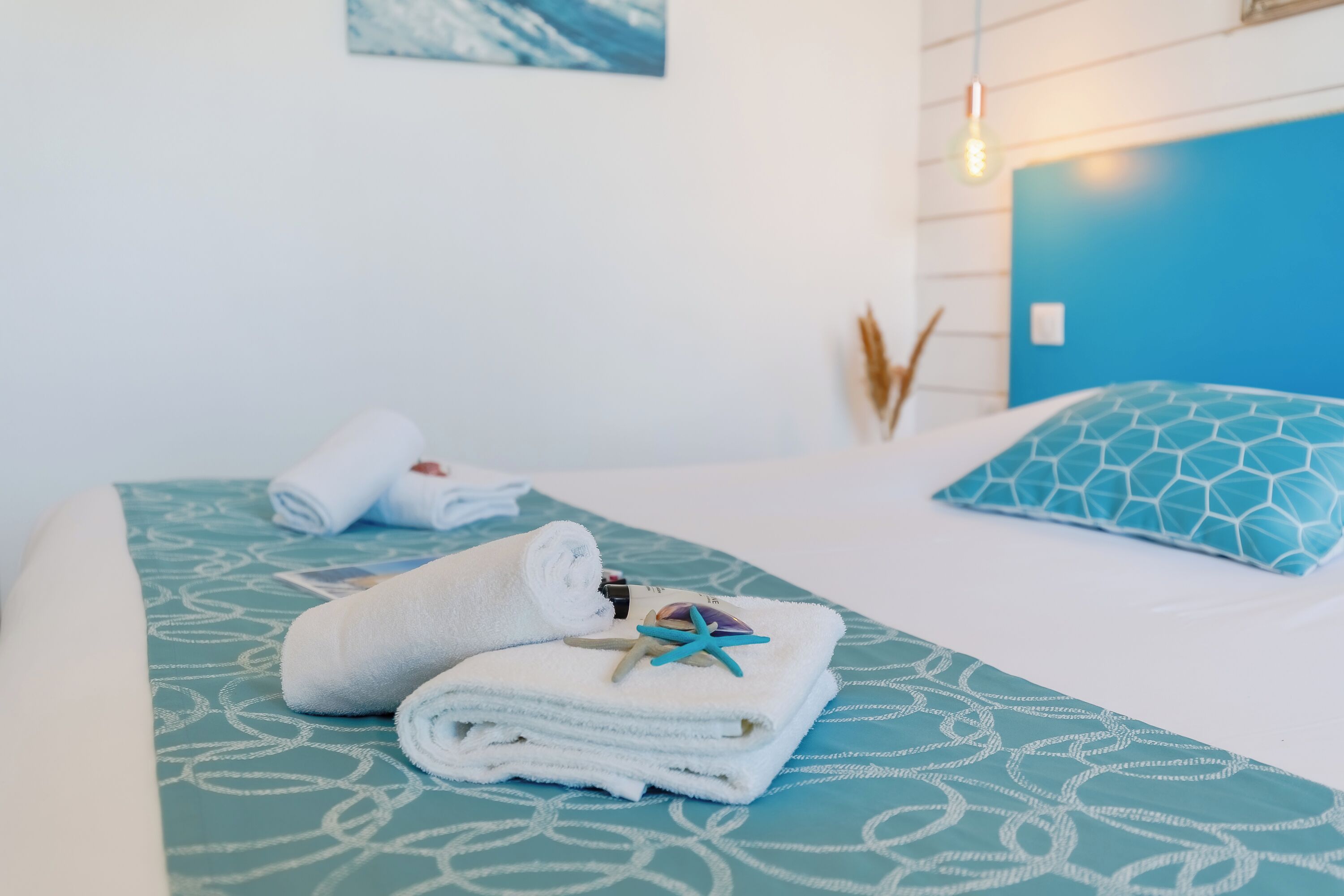 Una cama bien hecha con una colcha azul y blanca estampada, una almohada azul y toallas blancas enrolladas decoradas con una estrella de mar.