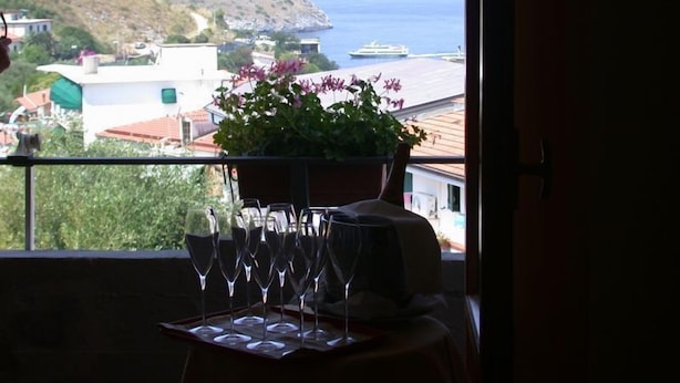 Ein Balkon mit Topfpflanze und Weingläsern, mit Blick auf eine Küstenstadt und das Meer.