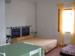 A bedroom with a bed, a small table, a nightstand, and a window with curtains.