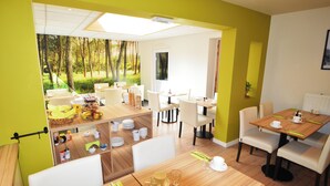 A dining area with multiple tables and chairs, a view of a forest through a large window, and a bright yellow wall. - Hotel Ambrosia (Ypres)