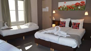 A hotel room with two single beds, a large bed, a painting of flowers, and a window with curtains.