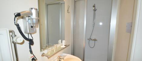A bathroom with a sink, mirror, hairdryer, and shower.
