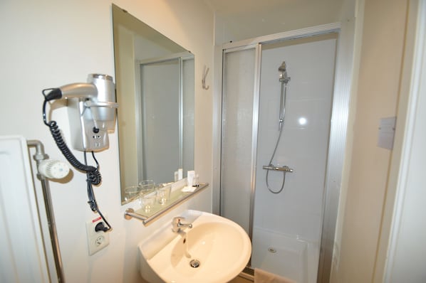 A bathroom with a sink, mirror, hairdryer, and shower. - Hotel Ambrosia (Ypres)