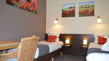 A hotel room with two beds, a wooden table, wicker chairs, and artwork on the walls.
