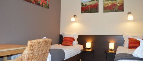 A hotel room with two beds, a wooden table, wicker chairs, and artwork on the walls.