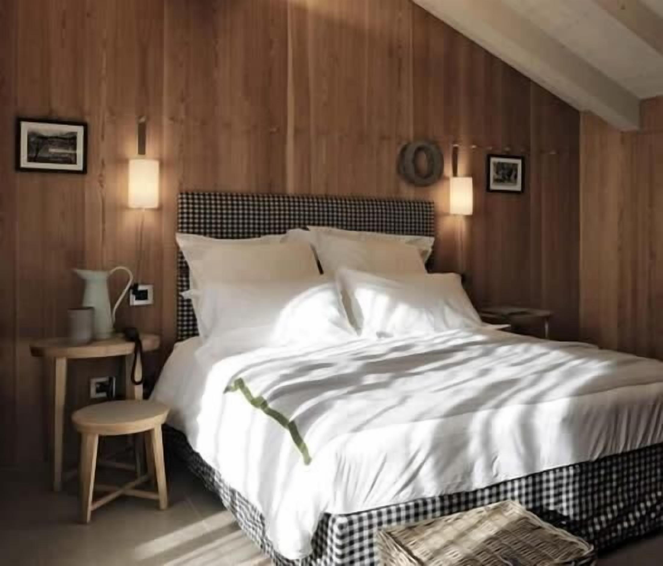 Camera da letto con parete in legno, copripiumino a quadretti, comodino con lampada e un piccolo sgabello.