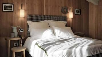 Camera da letto con parete in legno, copripiumino a quadretti, comodino con lampada e un piccolo sgabello.