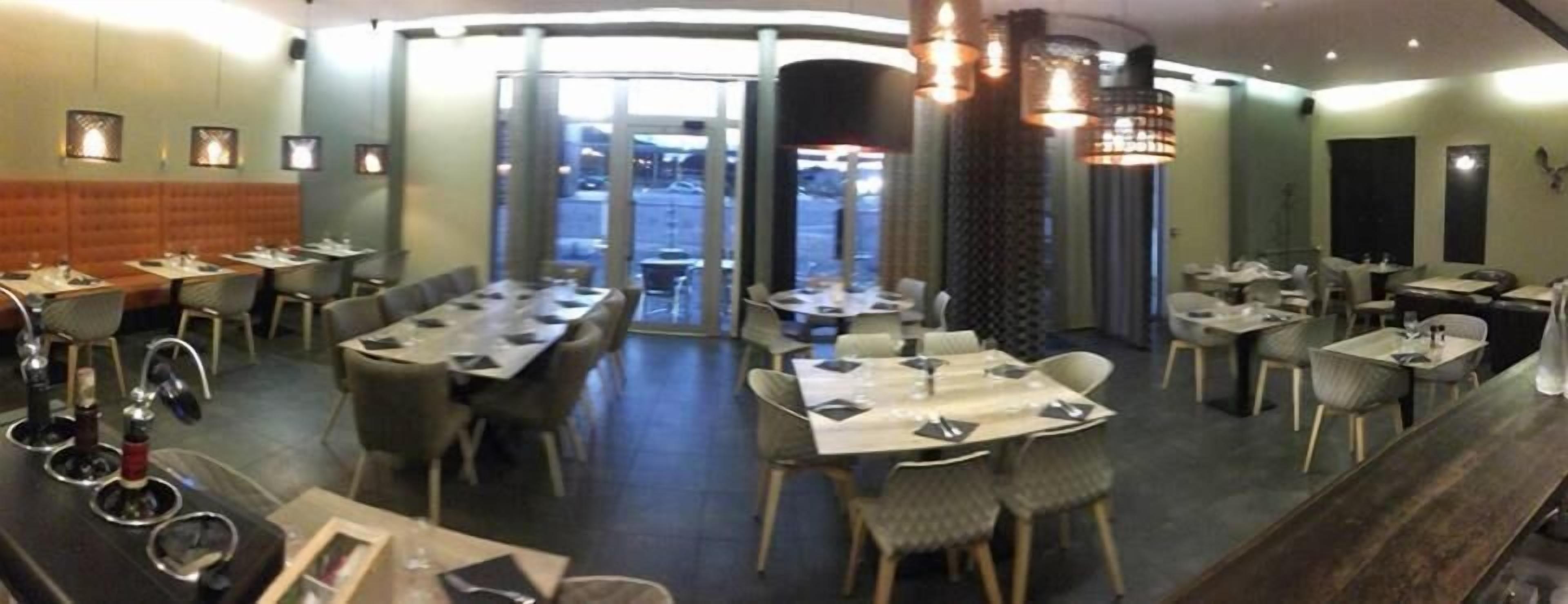 Un restaurante con varias mesas y sillas, una zona de bar con taburetes y vistas a la calle a través de amplios ventanales.