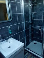 Un baño con lavamanos blanco, espejo y zona de ducha con puerta de vidrio.
