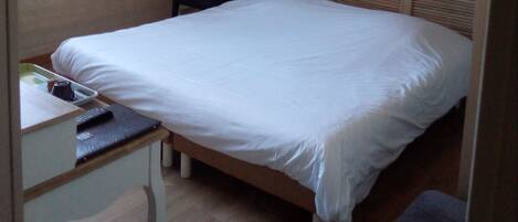 Un dormitorio con cama, escritorio, silla y televisor montado en la pared.