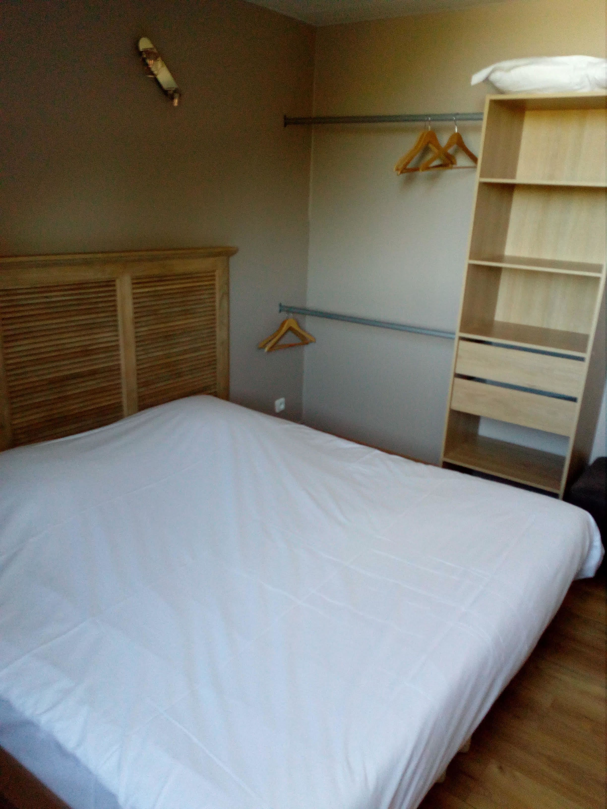 Quarto com cama, cabeceira de madeira, guarda-roupa com espelho e um cabideiro.