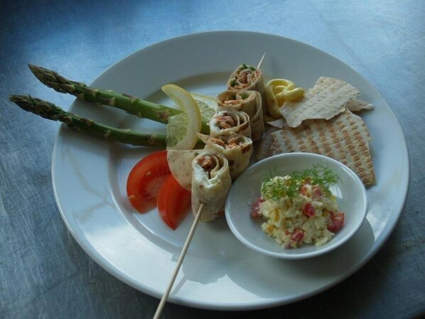 A plate with rolled sushi, asparagus, lemon slices, a tomato, crackers, and a small bowl of salad.