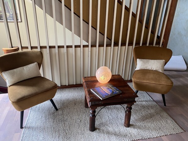 A room with two brown armchairs, a wooden coffee table with a book and a lamp, and a staircase in the background.