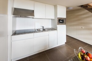 Una cocina con armarios blancos, un lavamanos de acero inoxidable y un microondas.