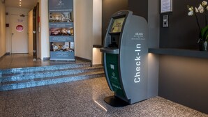 A hotel reception area with a check-in machine, a staircase, and a signboard displaying room types. - Arass Hotel & Business Flats (Antwerp)