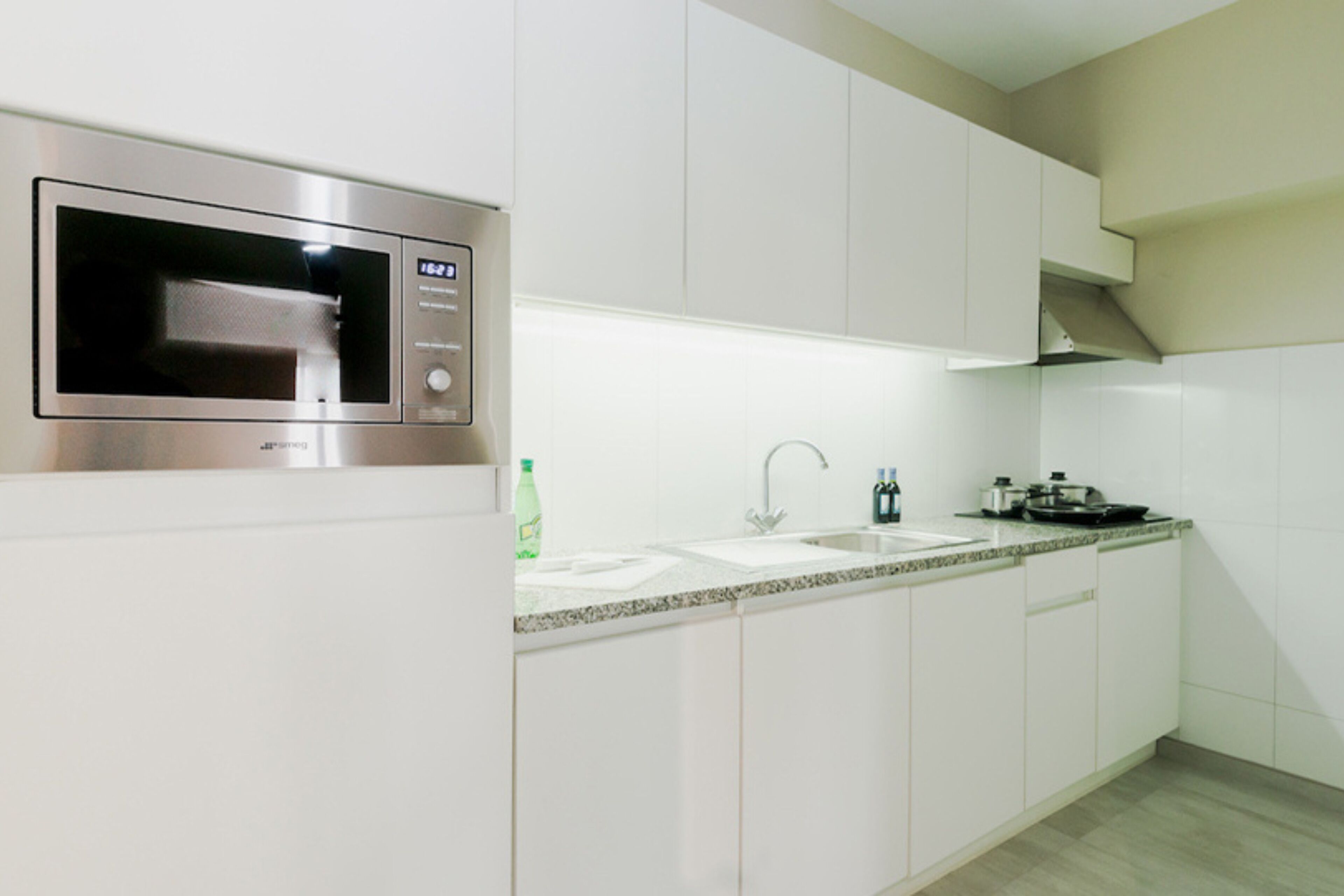 Een moderne keuken met witte kastjes, een roestvrijstalen magnetron, een dubbele spoelbak en een granieten aanrechtblad.