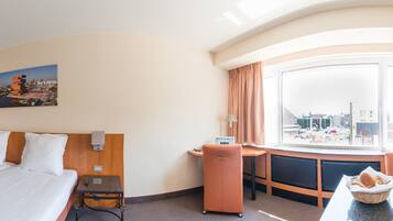 A hotel room with a bed, a desk, a chair, a window with a view of the city, and a small table with a basket of pastries.