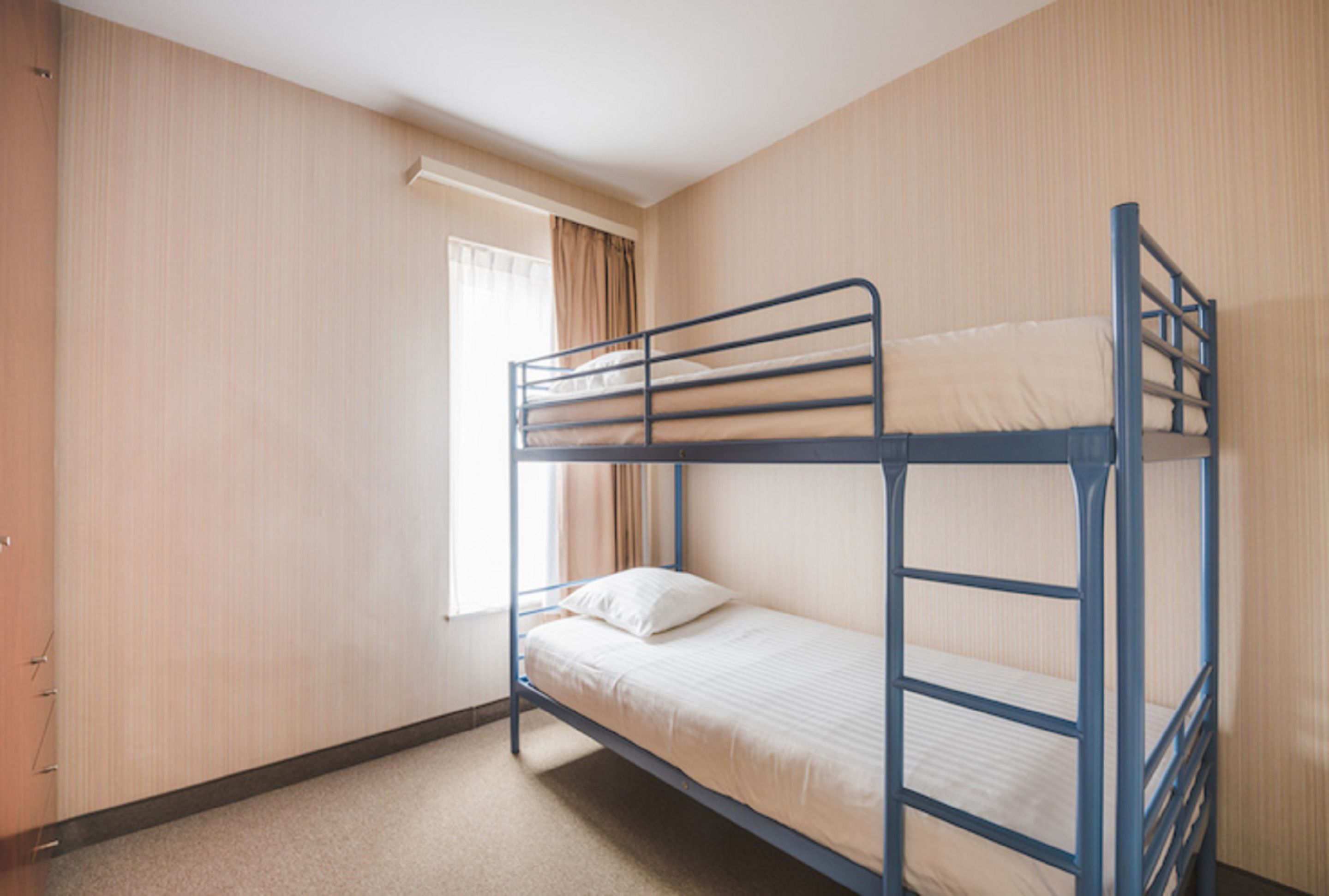 Quarto com beliche, janela, cortinas e porta.