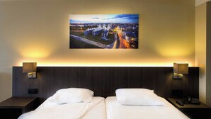 A hotel room with a large bed, two bedside tables, a nightstand, and a wall-mounted painting of a cityscape. - Arass Hotel & Business Flats (Antwerp)