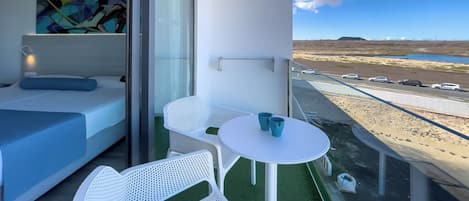 A balcony with a bed, white chairs, and a table with blue cups.