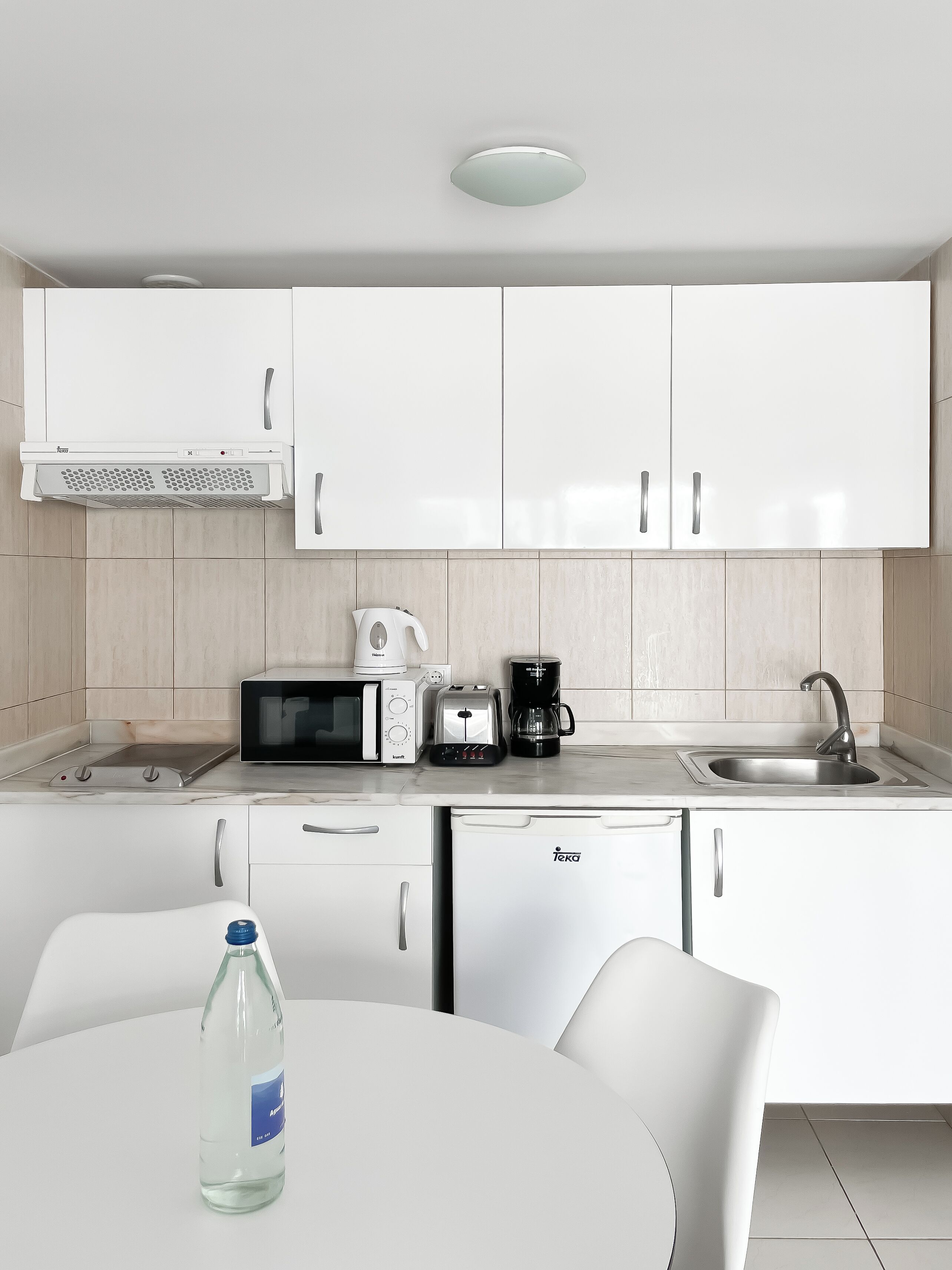 Una cocina moderna con armarios blancos, microondas, tostadora, cafetera y lavavajillas.