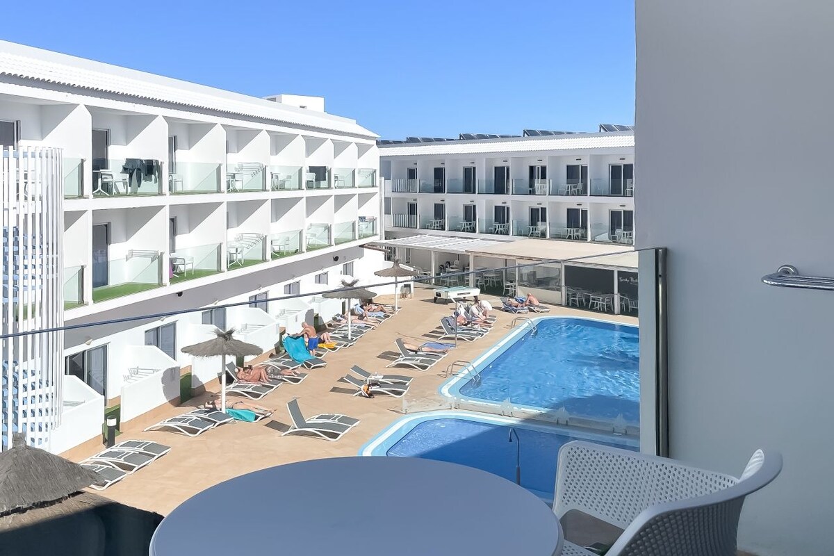 Un balcone d'hotel con piscina, poltrone a sdraio e un tavolo.