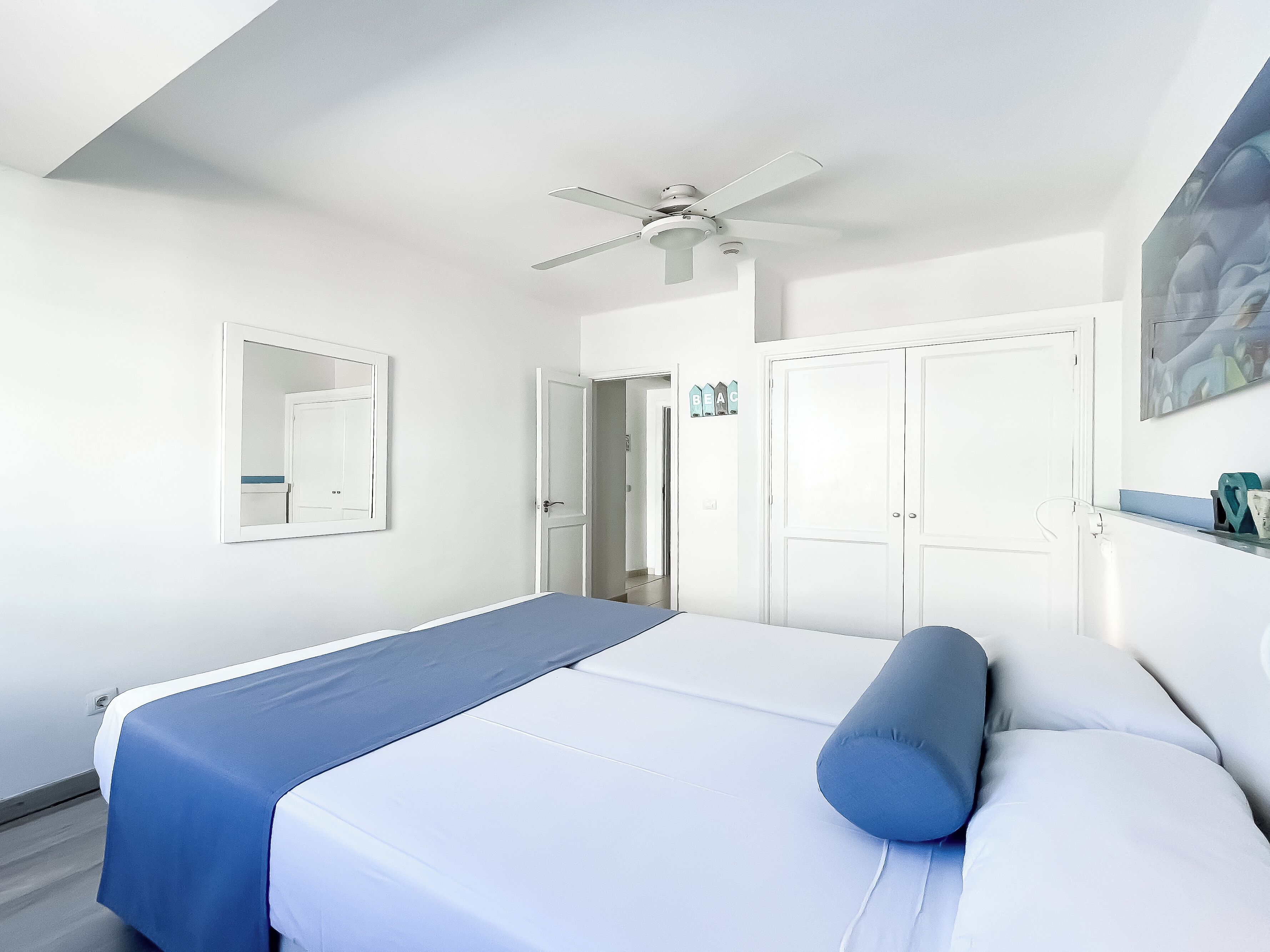 A bedroom with a bed, a ceiling fan, a door, and a wall-mounted mirror.