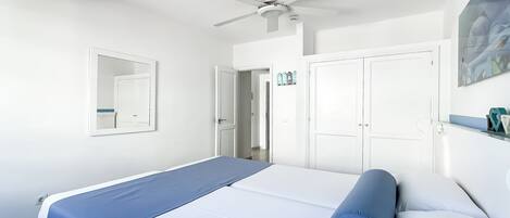 A bedroom with a bed, a ceiling fan, a door, and a wall-mounted mirror.