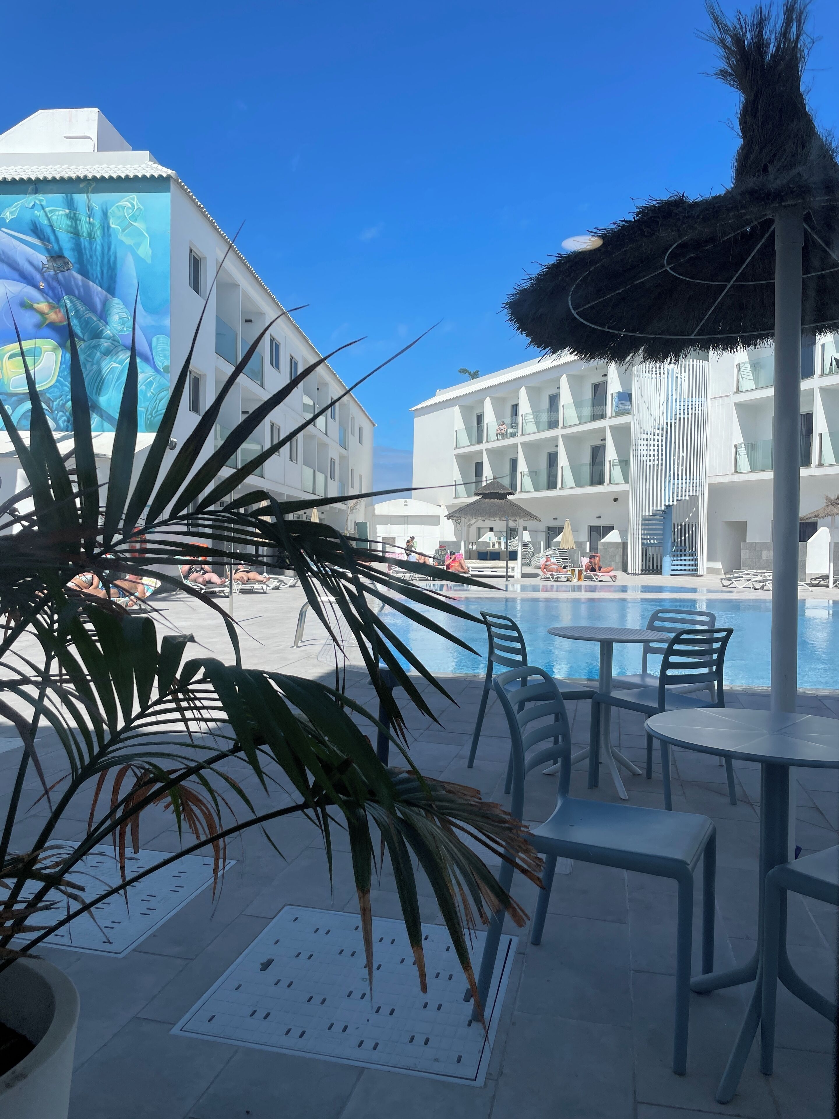 A pool area with lounge chairs and umbrellas, surrounded by white buildings with balconies.