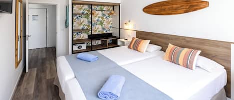 Une chambre d’hôtel comprenant un lit, une tête de lit en bois, une table de chevet et une étagère murale ornée d’un motif de feuilles tropicales, ainsi qu’un objet en bois accroché au mur.