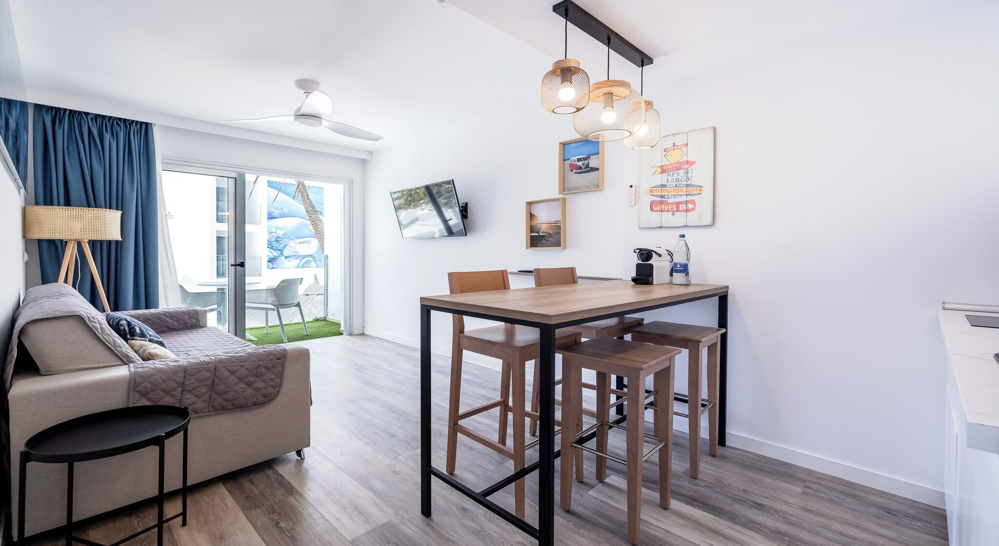 Un salon moderne comprenant un canapé, une table à manger avec des chaises, un ventilateur de plafond et une grande fenêtre avec des rideaux.