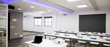 A conference room with white tables, blue folders, a laptop, and a projector.