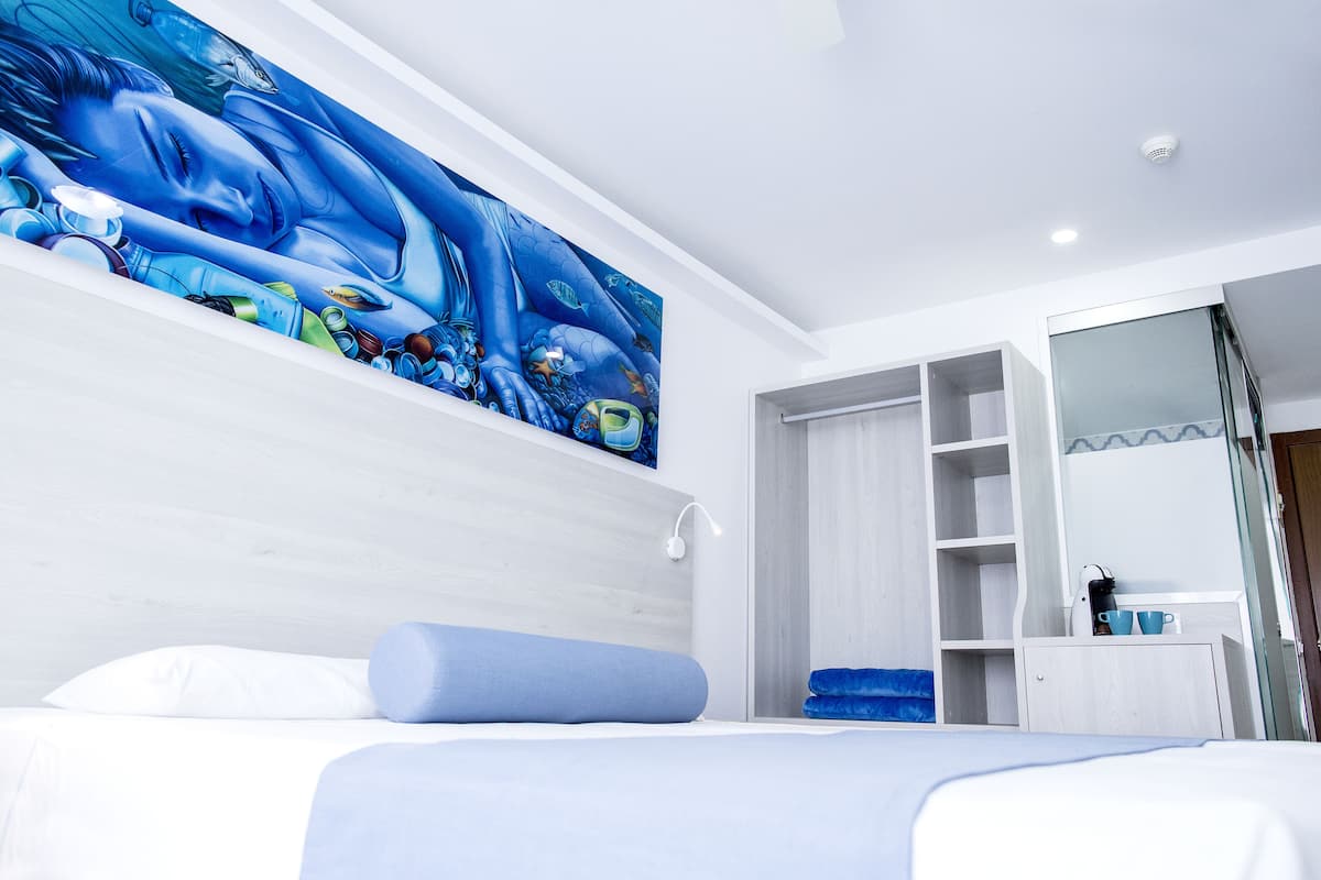 A modern hotel room with a large blue mural on the wall, a neatly made bed, and a walk-in closet.
