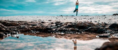 A person performing a yoga pose on a rocky beach with a clear sky.