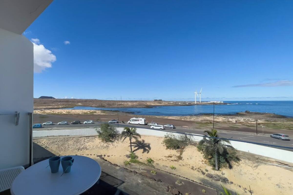 A balcony with a view of a coastal road, beach, and wind turbines.